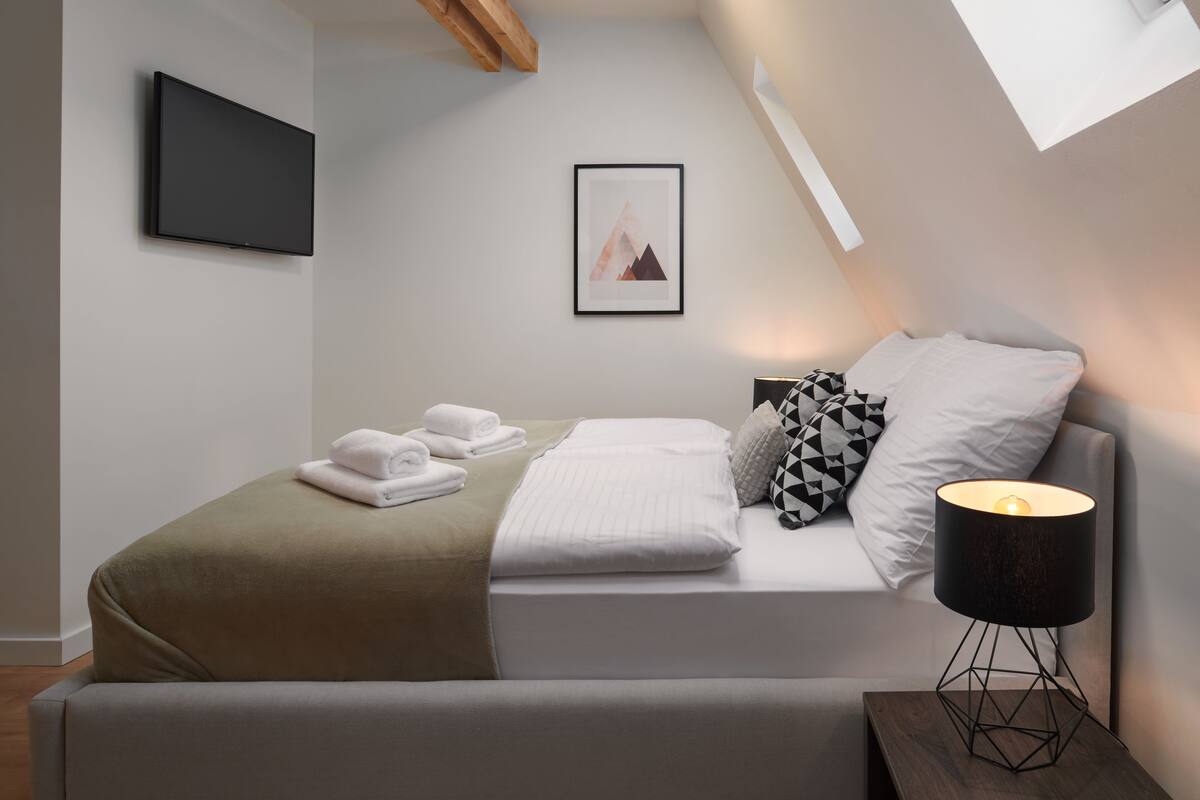 A modern bedroom with a bed, a bedside lamp, a framed picture on the wall, and a flat-screen TV.