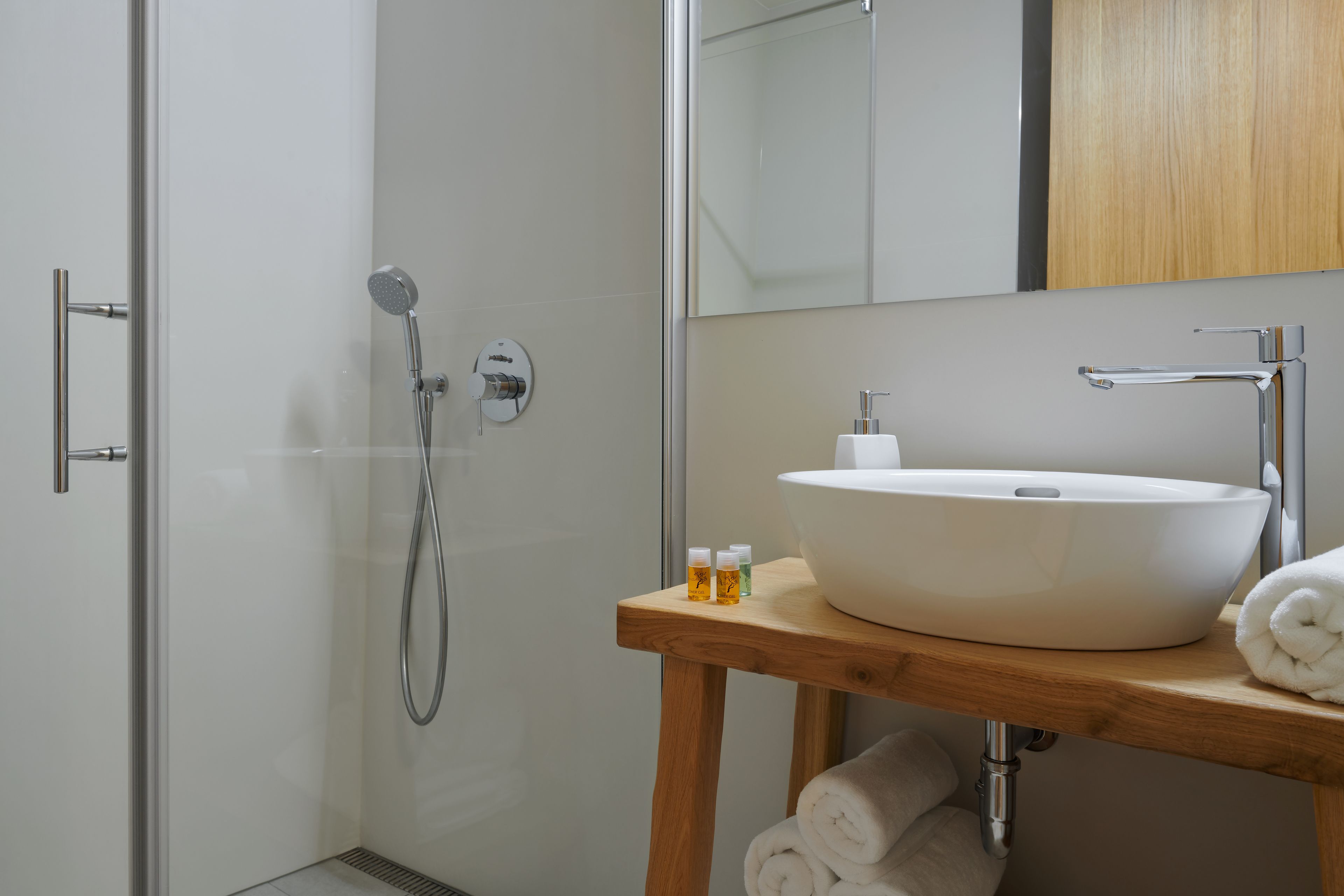 Une salle de bain moderne dotée d’une douche à parois de verre, d’un meuble-lavabo en bois avec un lavabo blanc et d’un miroir au-dessus du lavabo.