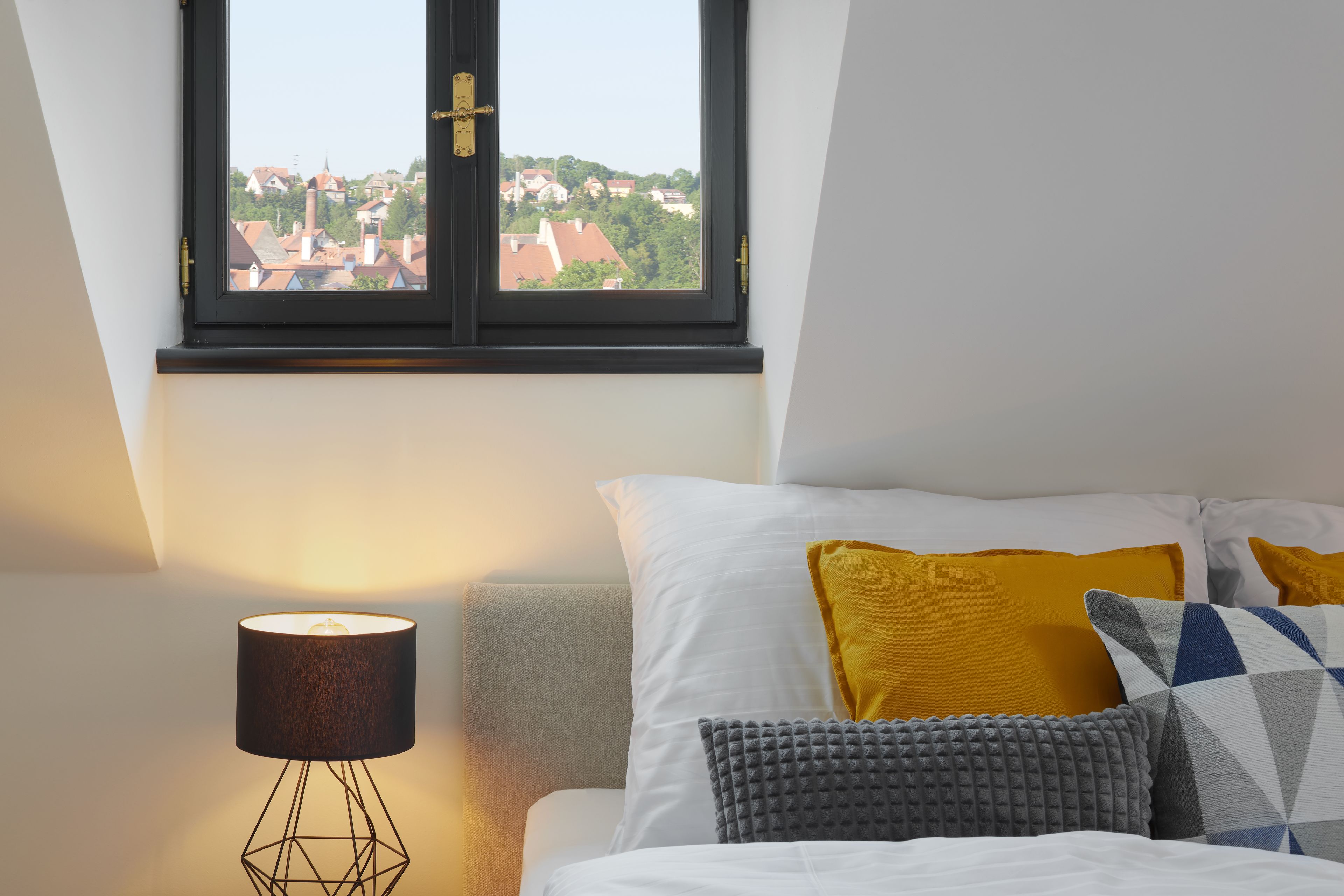 A bedroom with a bed, pillows, a lamp, and a window with a view of buildings.