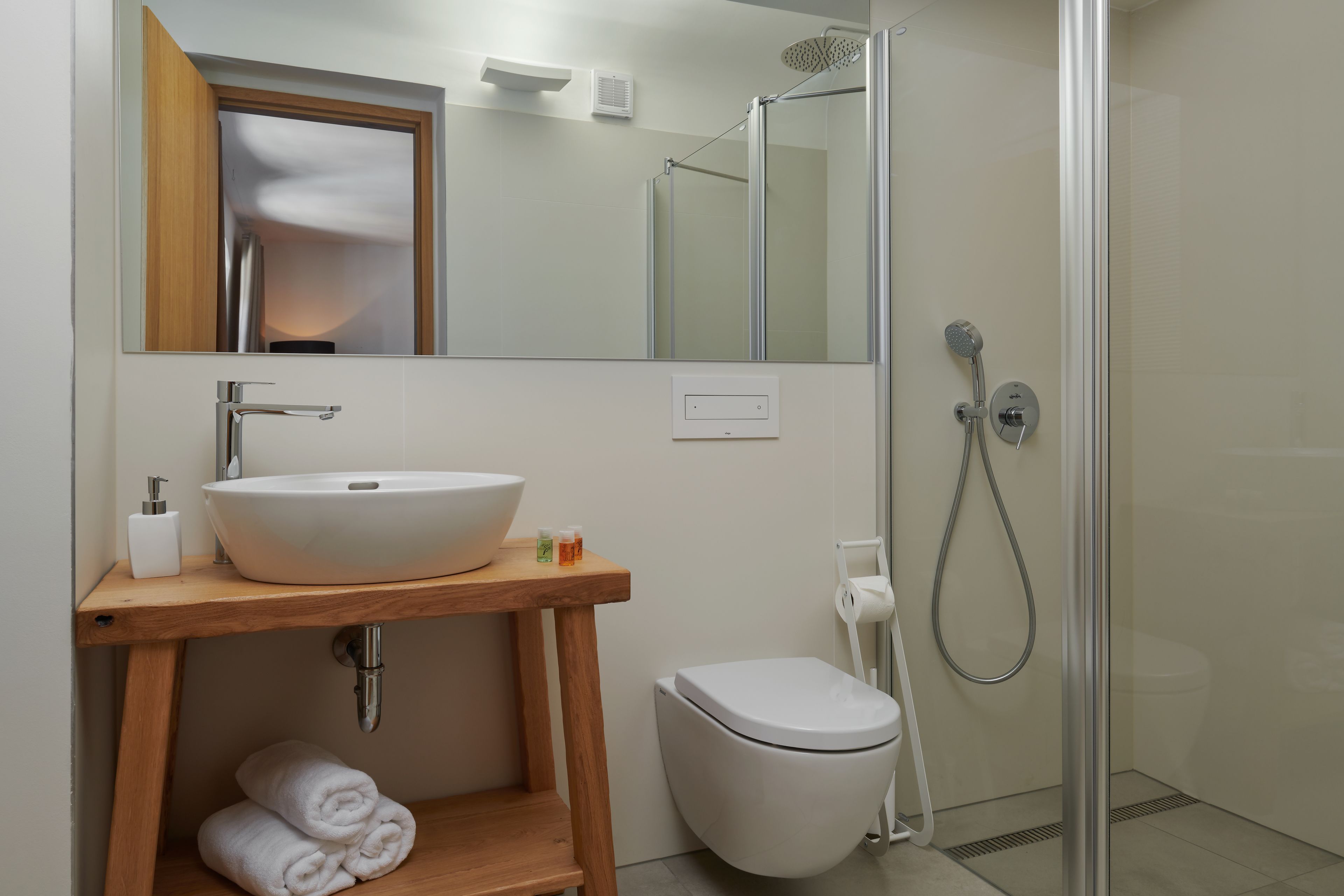Un baño con tocador de madera, lavabo blanco y cabina de ducha con mampara de vidrio.