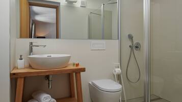 Un baño con tocador de madera, lavabo blanco y cabina de ducha con mampara de vidrio.