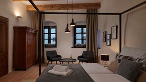 Un dormitorio con una cama grande, dos sillas, una mesita, un armario y ventanas con cortinas.