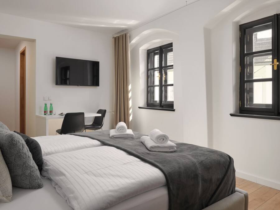 A hotel room with a bed, a desk, a chair, a TV, and a window.