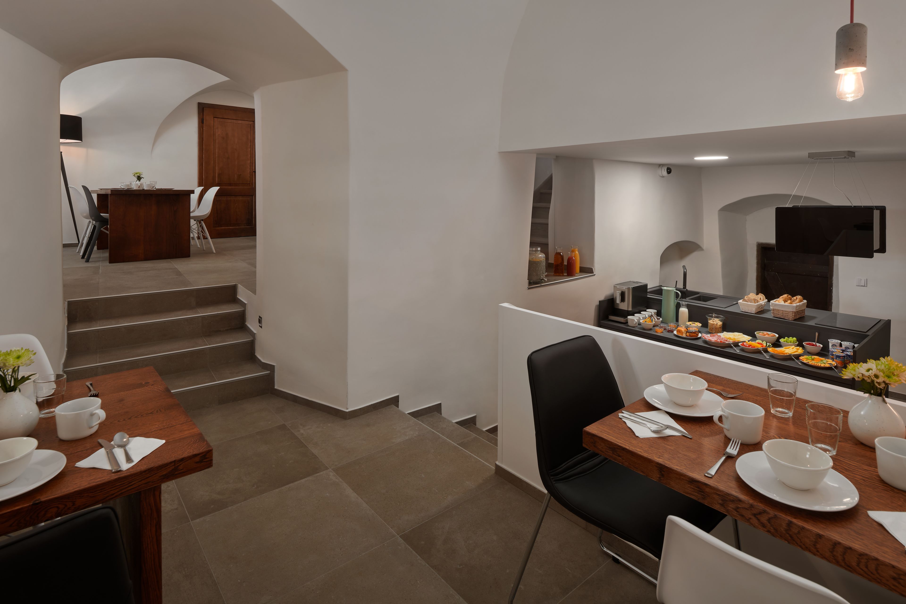 Una cocina moderna con zona de comedor, que incluye una mesa de madera, sillas blancas y una escalera que lleva a otra habitación.