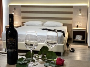 Habitación de hotel con una cama, mesitas de noche, una botella de vino, dos copas de vino y una rosa.