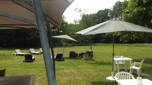 An outdoor seating area with tables and chairs under umbrellas, surrounded by grass and trees. - Le Domaine de Jaugy - Hostel (Gievres)