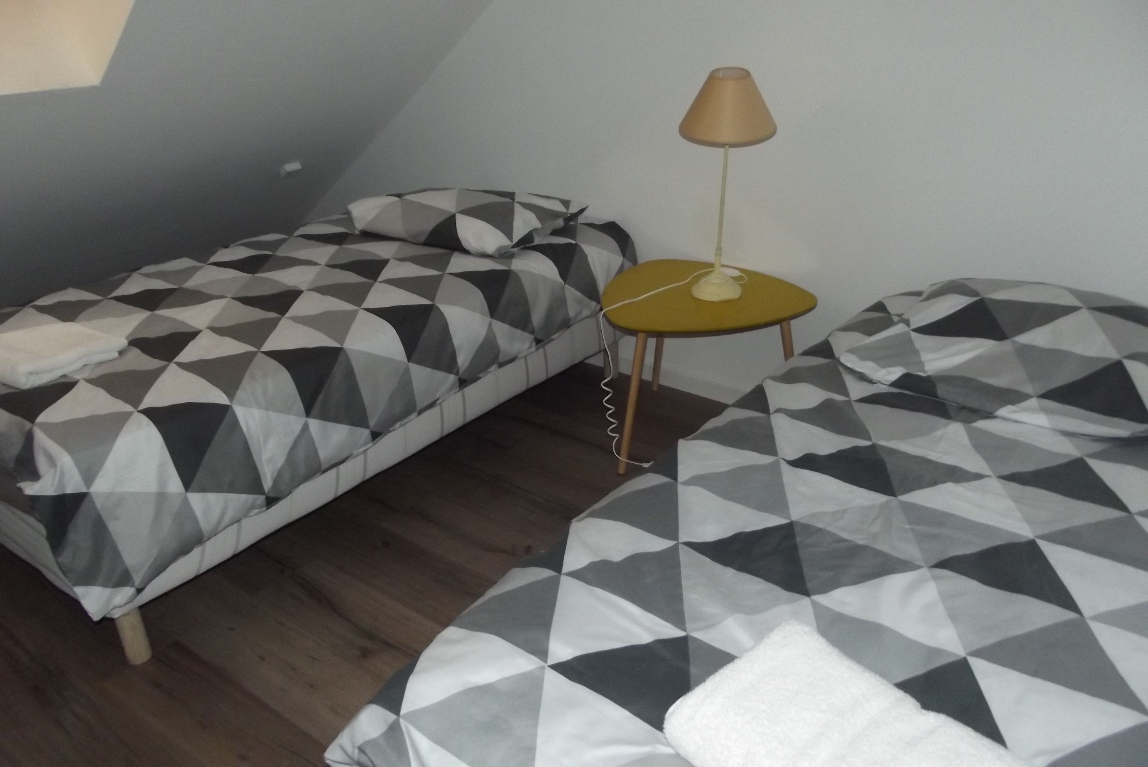 Een kleine, eenvoudige kamer met twee bedden, een tafeltje en een lamp.