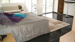 Une chambre moderne avec un grand lit, un canapé et une vue sur l’extérieur grâce à une porte-fenêtre coulissante.