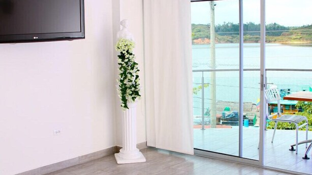 Une chambre moderne dotée d’une grande porte-fenêtre coulissante qui donne sur un balcon offrant une vue sur un plan d’eau et la verdure.