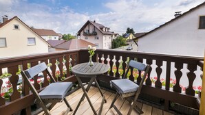 Une terrasse en bois avec deux chaises et une table, donnant sur un quartier résidentiel avec des maisons et un ciel dégagé.