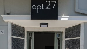 Rakennuksen sisäänkäynti, jonka yläpuolella olevassa kyltissä lukee: ”huoneisto 27”.
