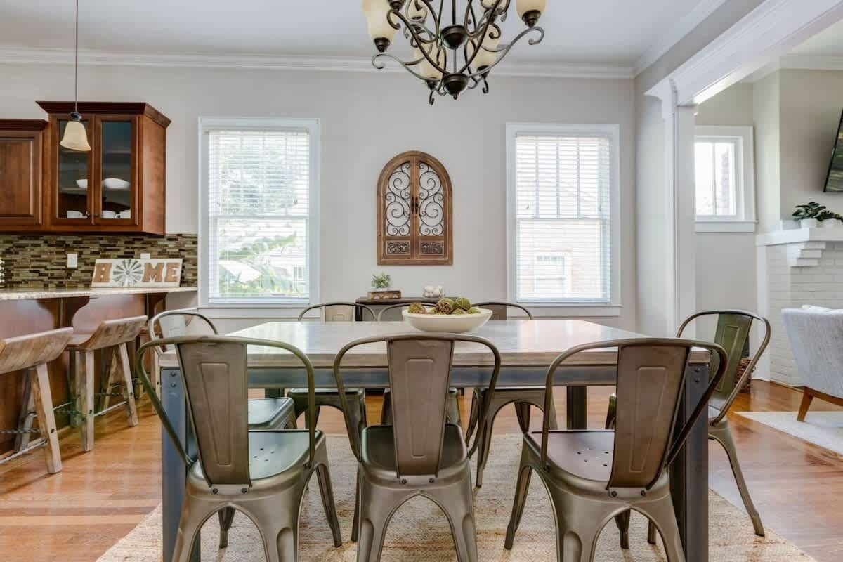 A dining area with a large table, metal chairs, a chandelier, and a view of the outdoors through windows.