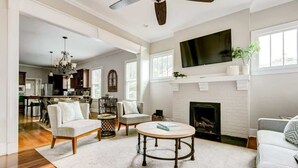 A spacious living room with a fireplace, a ceiling fan, and a television mounted above it.
