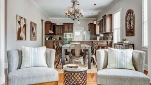 A spacious living room with a dining area, featuring a chandelier, wooden cabinets, and artwork on the walls.