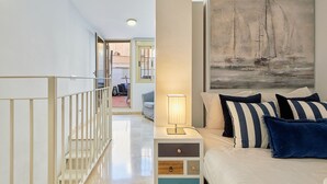 A bedroom with a bed, a nightstand with a lamp, a painting of a sailboat, and a view of the outside balcony. - Hanna - Holiday rental Malaga City (Málaga)