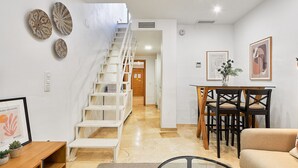 A modern interior with a staircase leading to a second floor, a dining area with a table and chairs, and a living space with a sofa and decorative items. - Hanna - Holiday rental Malaga City (Málaga)