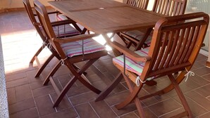 A covered patio with a wooden table and chairs, large windows, and a view of buildings. - Apartment in Torre Valentina, 2 min from the beach (Calonge)