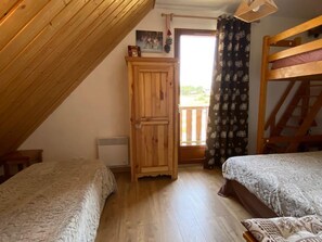 Une chambre avec deux lits, une armoire en bois, un radiateur et une fenêtre avec des rideaux.