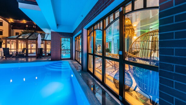 A modern hotel lobby with a swimming pool, large windows, and a glass-enclosed area with a decorative structure.
