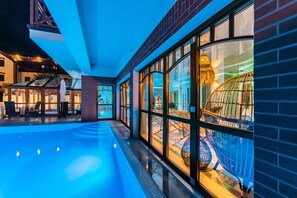 Un hall d’hôtel moderne doté d’une piscine, de grandes fenêtres et d’un espace clos par des parois de verre, agrémenté d’une structure décorative.