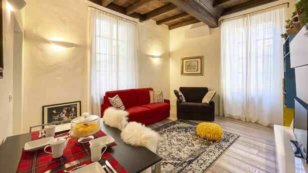A cozy living room with a red sofa, a black armchair, and a yellow pouf on a patterned rug. - LuxRent Apartment Castello (Torino)