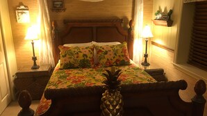 A bed with a floral bedspread, two nightstands with lamps, a decorative pineapple centerpiece, and a wooden headboard.