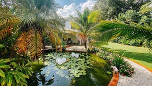 A serene garden with a pond, lush greenery, and a small building.