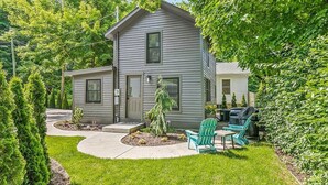A two-story house with a front porch, a small garden, and a grill area. - Singapore Stable hot tub walk to Saugatuck! (Saugatuck)
