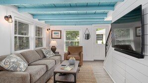 A living room with a sofa, armchair, coffee table, and a TV mounted on the wall. - Singapore Stable hot tub walk to Saugatuck! (Saugatuck)