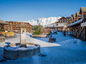 Stroll through the serene snow-covered courtyard, surrounded by traditional chalet-style buildings and a tranquil stone fountain.