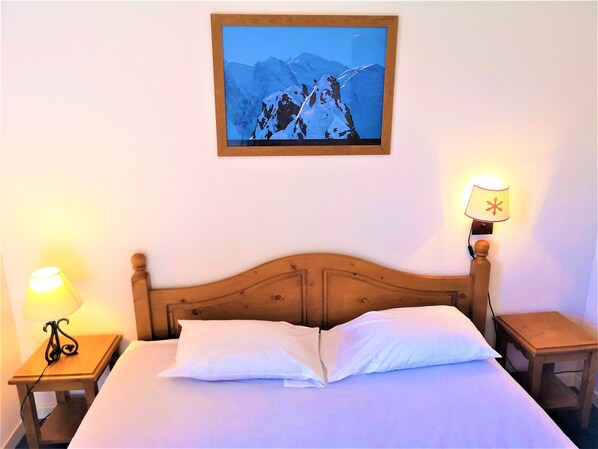 Habitación de hotel con cama de madera, dos lámparas de noche, un cuadro enmarcado de una montaña y una mesita de noche.