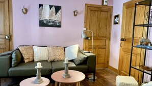 A cozy living room with a green sofa, a pink table, and a patterned rug. - Large charming refuge at the water's edge in Gérardmer. Spa / sauna / Wifi (Gérardmer)
