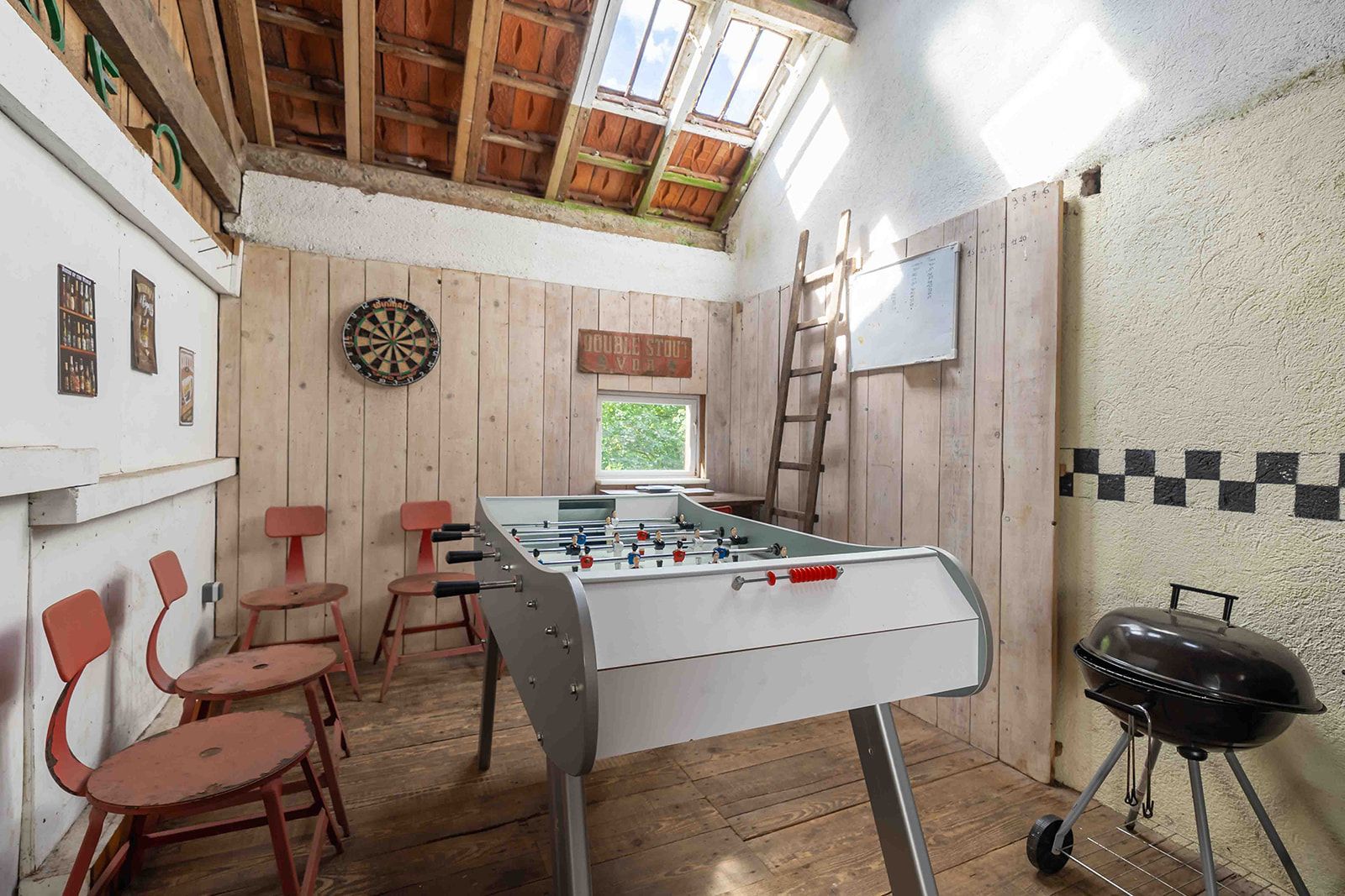 A room with a foosball table, a dartboard, and a foosball table with a window view.