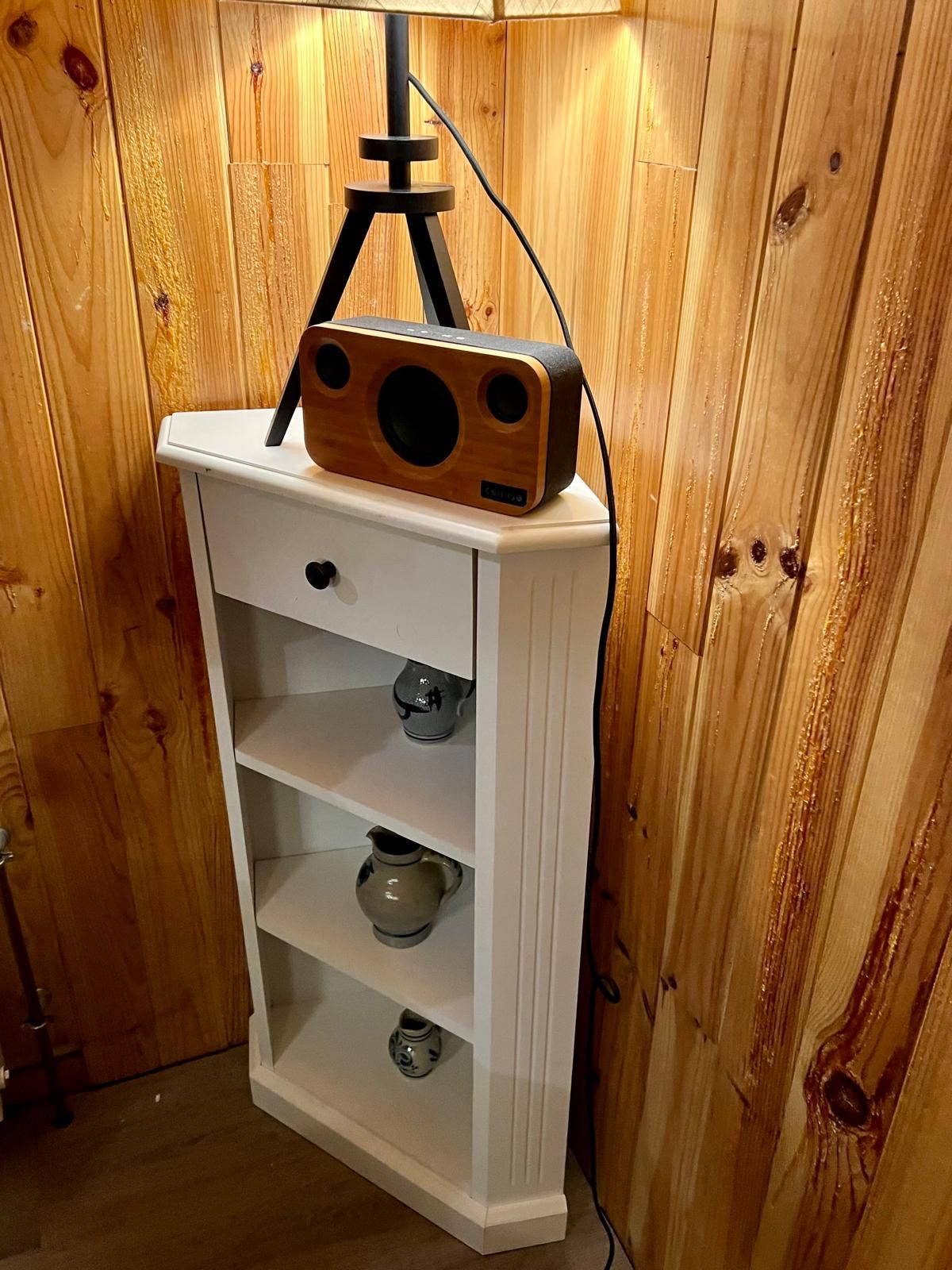 Ein weißes Schränkchen mit einem Holzradio obenauf, Regale mit Keramikgegenständen und einem Holzpaneel als Hintergrund.