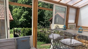 A sunroom with a view of a forest, a wooden table with chairs, and a bench with cushions. - Large charming refuge at the water's edge in Gérardmer. Spa / sauna / Wifi (Gérardmer)
