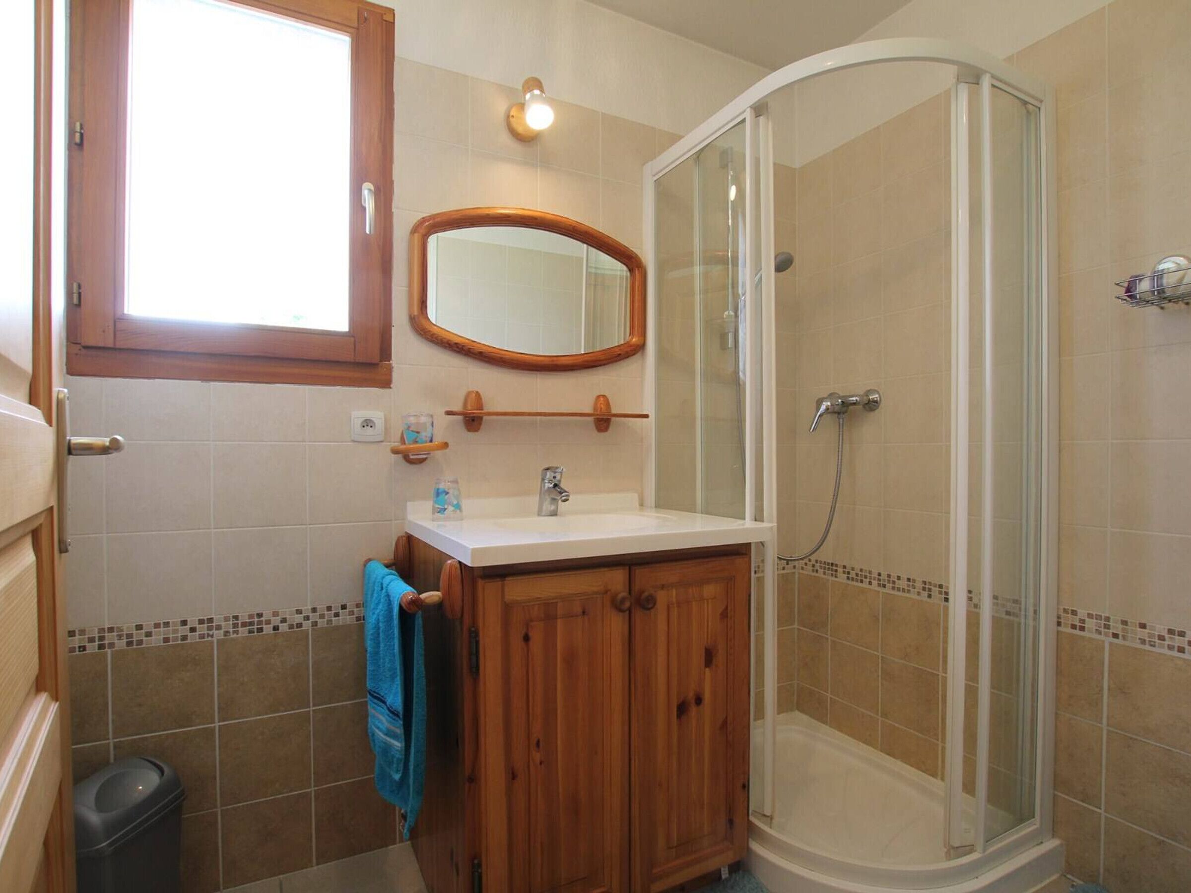 A bathroom with a wooden vanity, a mirror, a shower enclosure, and a tiled floor.