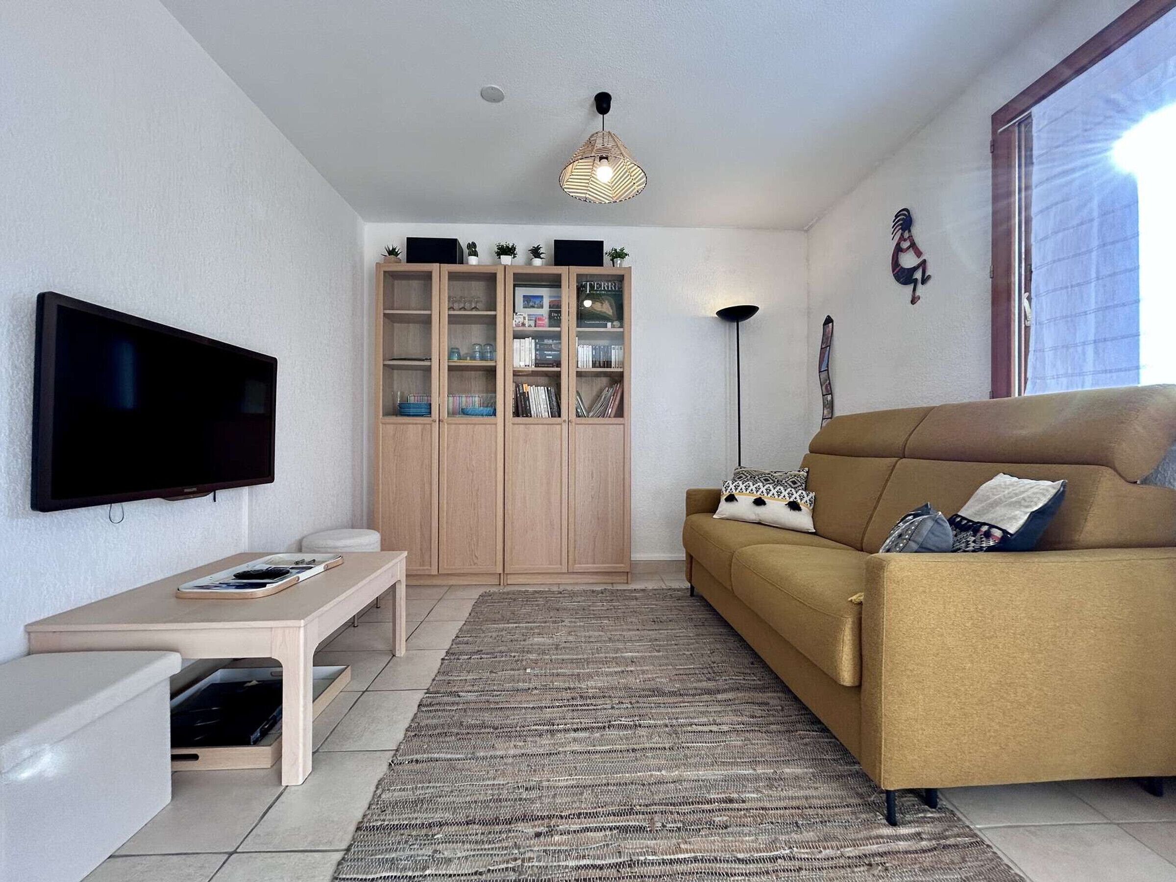 Una sala de estar con una televisión de pantalla plana, un mueble de madera, un sofá y una lámpara de pie.