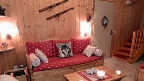 Une pièce chaleureuse avec des murs en bois, un canapé rouge, une table basse en bois ornée de bougies et un escalier.