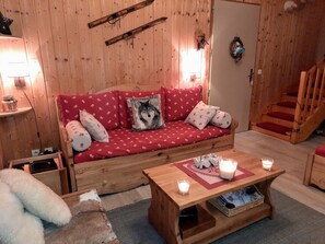 A cozy wooden room with a red sofa, a wooden coffee table with candles, and a staircase. - Renovated chalet for 6 with WIFI and free parking in La Joue du Loup (La Joue du Loup)
