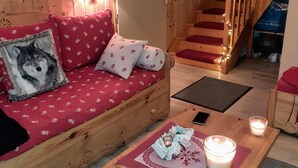 Un intérieur chaleureux avec des éléments en bois, un canapé rouge à motifs, un escalier en bois avec des marches rouges et une bougie posée sur une table.