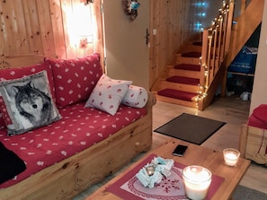 A cozy wooden interior with a red patterned sofa, a wooden staircase with red steps, and a candle on a table.