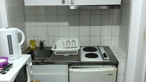 Een kleine keuken met een magnetron, een kleine koelkast, een fornuis en een spoelbak.