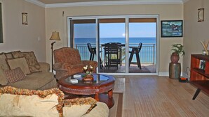Un salon comprenant un canapé, un fauteuil et une table basse, un balcon avec une table et des chaises, et une vue sur l’océan.