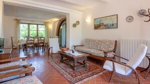 A spacious living room with a wooden coffee table, floral sofa, and a dining area with a table and chairs. - Apartment "Piccolo paradiso" (Crespina, Pisa)