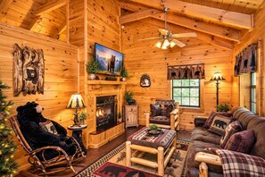 A log cabin interior with a fireplace, wooden furniture, a rocking chair, and a ceiling fan. - Mosey Bear, Hot Tub, WIFI, $560 FREE tickets each paid day!!! (Sevierville)