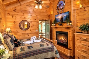 A cozy log cabin bedroom with a bed, a fireplace, a mirror, and a bear-themed wall decoration.
