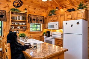 A cabin-style kitchen with wooden cabinets, a granite countertop, a bear-themed mug, and a bear statue. - Mosey Bear, Hot Tub, WIFI, $560 FREE tickets each paid day!!! (Sevierville)