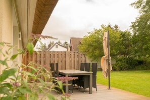 Une terrasse extérieure avec une table et des chaises, une terrasse en bois et une clôture en arrière-plan.