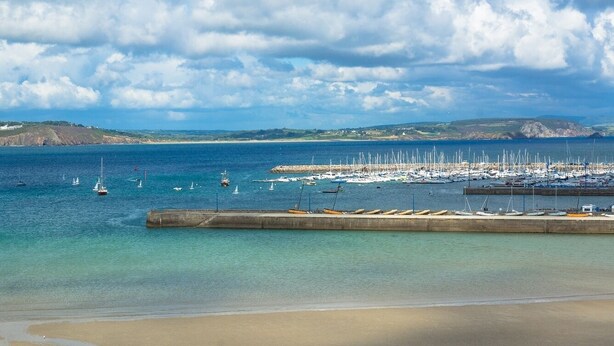 Un port de plaisance situé sur la côte, avec des bateaux amarrés et une plage de sable au premier plan.