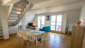 Un vaste espace de vie doté d’un plancher en bois, d’une table à manger avec des chaises, d’un fauteuil bleu, d’un escalier, d’une télévision et d’un globe terrestre posé sur un meuble.